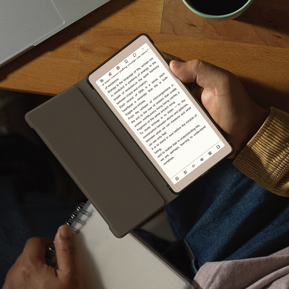 Person holding a viwoods AiPaper reader with a book open on the screen, sitting at a wooden table.